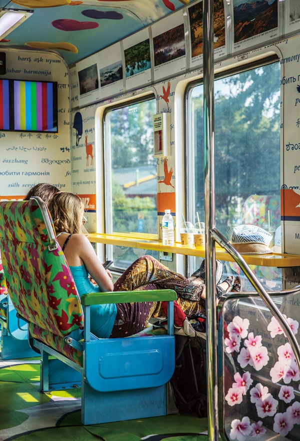 바람개비와 풍선, 연꽃이 내부에 그려진 DMZ열차. 두 외국인 여행객이 창밖을 내다보고 있다