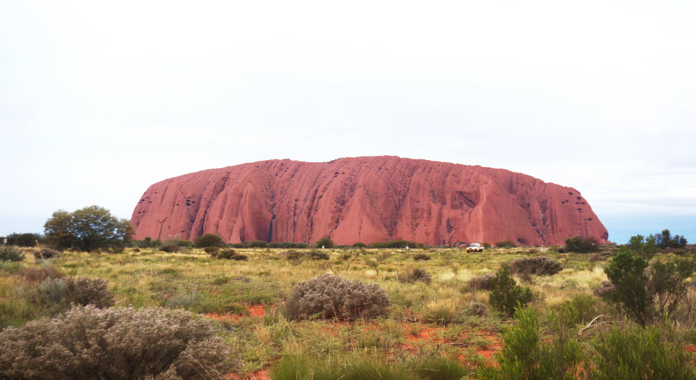 붉은 모래로 뒤덮인 사막 위에 단일 암석으로 이뤄진 거대한 울루루가 우뚝 솟아 있다.
